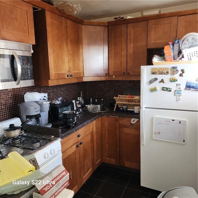 kitchen featuring backsplash, dark stone counters, white appliances, sink, and dark tile patterned flooring