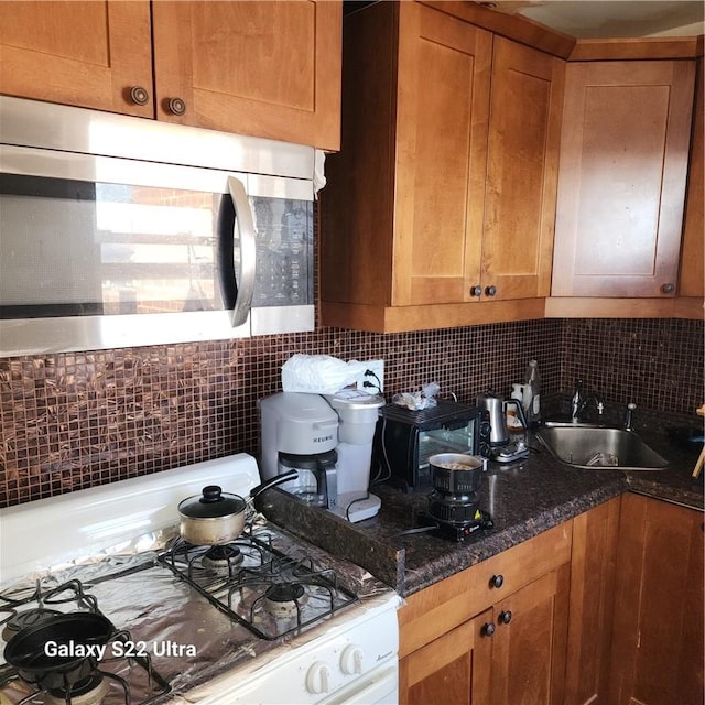 kitchen featuring range, backsplash, dark stone countertops, and sink