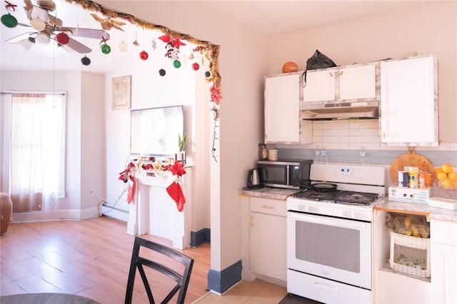 kitchen with light wood-type flooring, white gas range, baseboard heating, tasteful backsplash, and white cabinetry