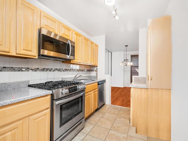 kitchen with appliances with stainless steel finishes, sink, light brown cabinets, light tile patterned floors, and hanging light fixtures