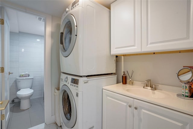 clothes washing area featuring light tile patterned flooring, sink, stacked washer and dryer, and tile walls