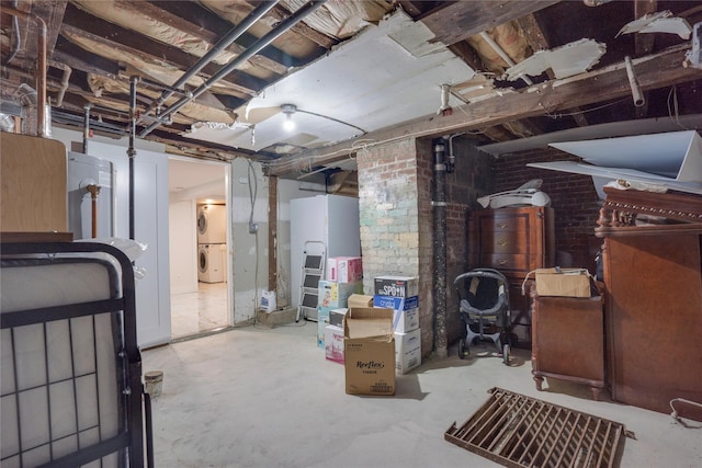 basement featuring stacked washing maching and dryer and brick wall