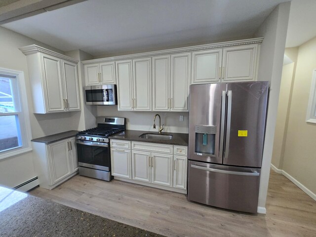 kitchen featuring white cabinetry, sink, stainless steel appliances, a baseboard radiator, and light wood-type flooring