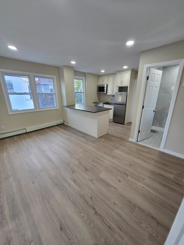 kitchen with kitchen peninsula, light wood-type flooring, stainless steel appliances, a baseboard radiator, and white cabinets