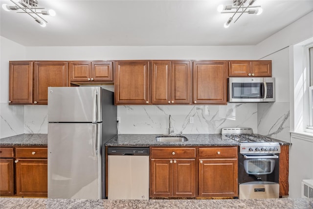 kitchen with appliances with stainless steel finishes, backsplash, dark stone counters, and sink