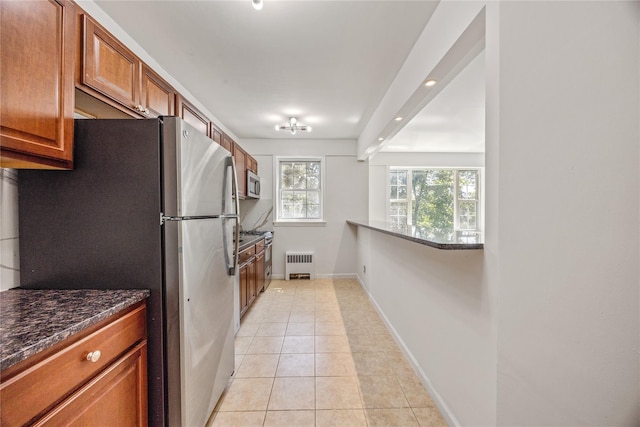 kitchen with radiator, light tile patterned floors, dark stone counters, and appliances with stainless steel finishes