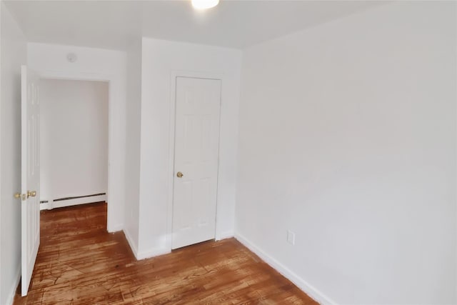 unfurnished bedroom with wood-type flooring and baseboard heating