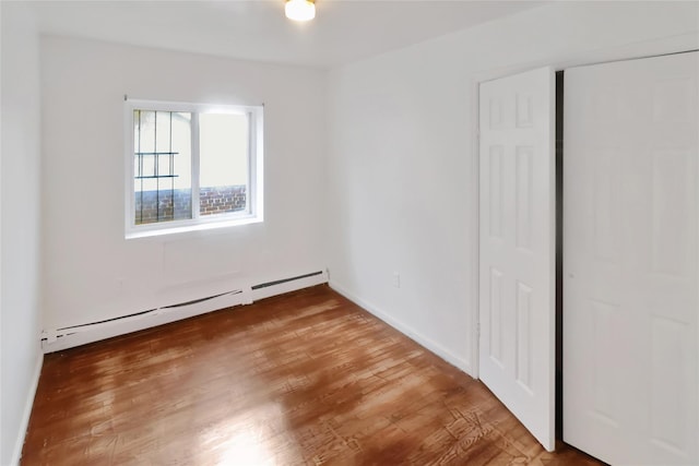 unfurnished bedroom with wood-type flooring and baseboard heating