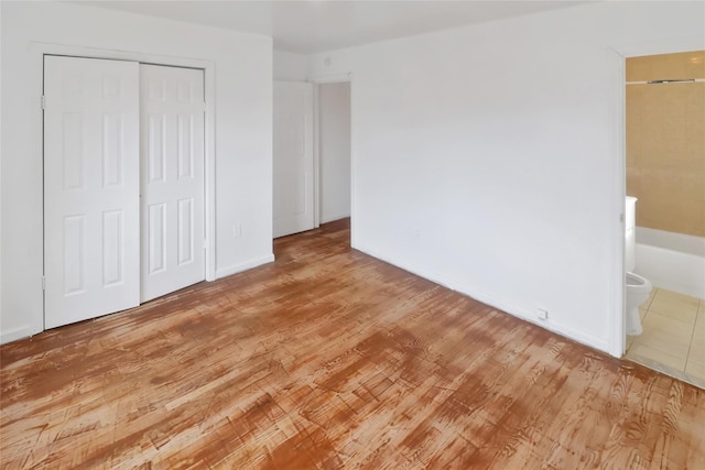 unfurnished bedroom with light wood-type flooring, a closet, and connected bathroom