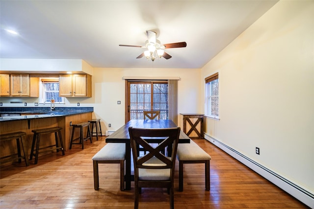 dining area featuring ceiling fan, light hardwood / wood-style flooring, sink, and a baseboard heating unit