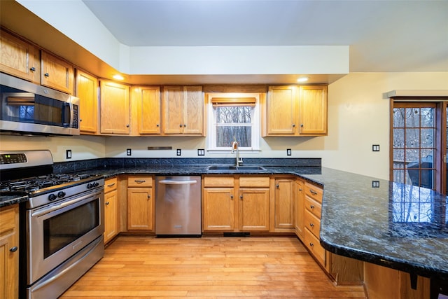 kitchen with sink, dark stone countertops, light wood-type flooring, appliances with stainless steel finishes, and kitchen peninsula