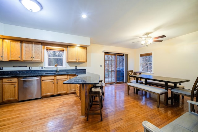 kitchen featuring a kitchen bar, ceiling fan, sink, light hardwood / wood-style flooring, and dishwasher