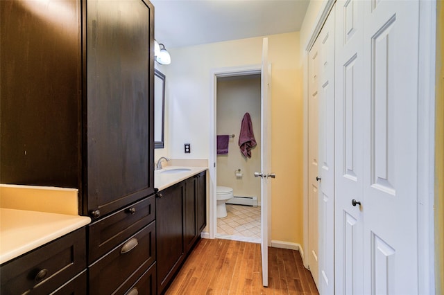 bathroom with toilet, hardwood / wood-style floors, vanity, and a baseboard heating unit