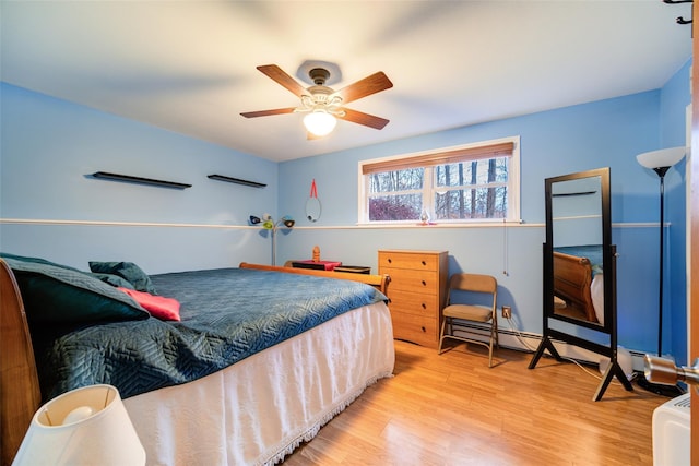 bedroom featuring ceiling fan, a baseboard heating unit, and light hardwood / wood-style flooring