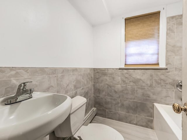 bathroom featuring a bathing tub, sink, tile walls, and toilet