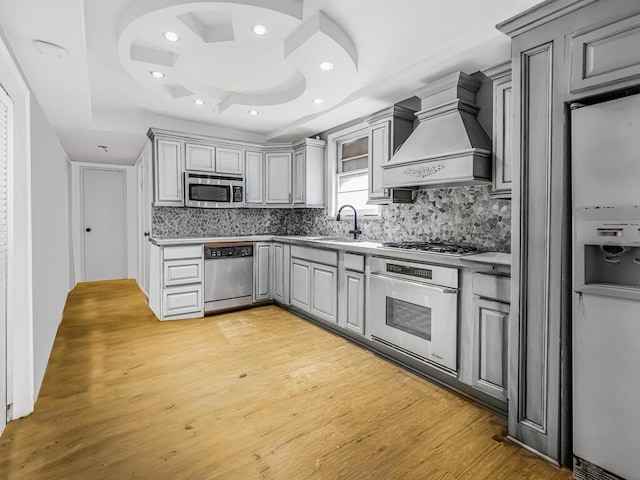 kitchen featuring a raised ceiling, light wood-type flooring, premium range hood, and appliances with stainless steel finishes