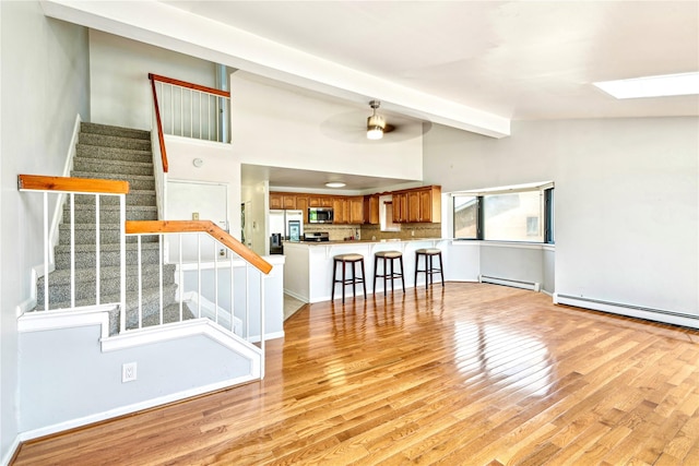 unfurnished living room with a baseboard radiator, light hardwood / wood-style flooring, and lofted ceiling with skylight