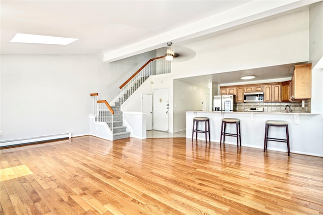 unfurnished living room featuring ceiling fan, light hardwood / wood-style floors, a baseboard heating unit, and a skylight