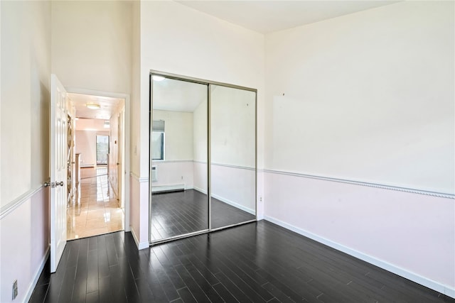 unfurnished bedroom with baseboard heating, dark wood-type flooring, and a closet