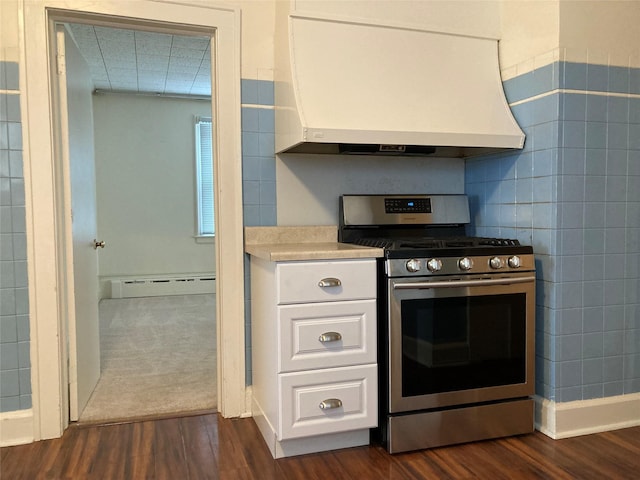 kitchen with stainless steel range with gas cooktop, white cabinets, wall chimney exhaust hood, baseboard heating, and dark wood-type flooring