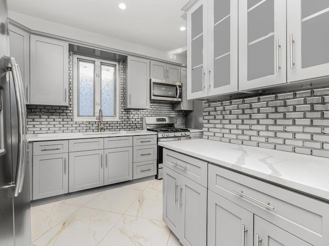 kitchen featuring sink, gray cabinets, light stone countertops, tasteful backsplash, and stainless steel appliances