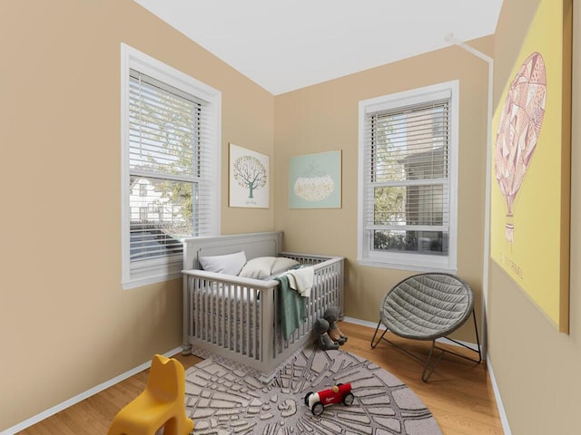 bedroom with a crib, light wood-type flooring, and multiple windows