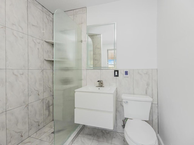 bathroom with a tile shower, vanity, toilet, and tile walls