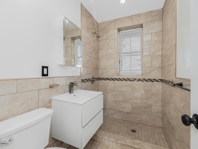 bathroom with a tile shower, vanity, tile walls, and toilet