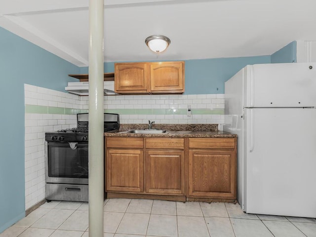 kitchen with gas stove, sink, backsplash, white fridge, and light tile patterned floors