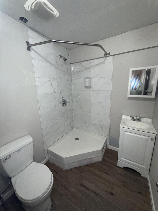 bathroom with toilet, wood-type flooring, vanity, and a tile shower