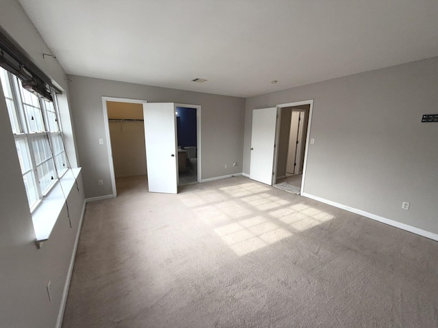 unfurnished bedroom featuring a closet, a spacious closet, light carpet, and ensuite bath