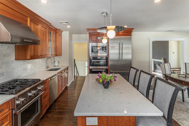 kitchen with a center island, glass insert cabinets, a sink, wall chimney range hood, and built in appliances