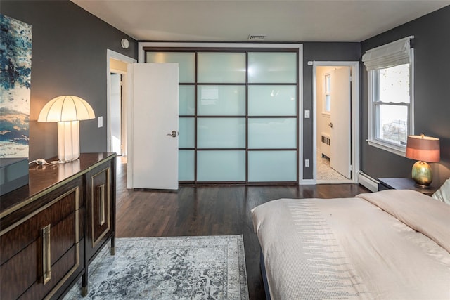 bedroom with dark wood finished floors, visible vents, radiator heating unit, ensuite bathroom, and a baseboard heating unit