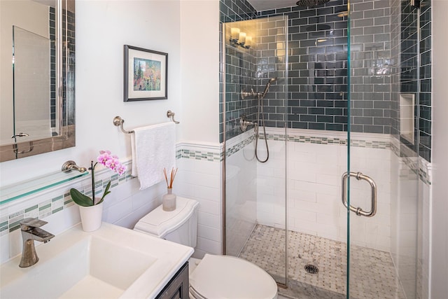 full bath with a wainscoted wall, tile walls, toilet, a stall shower, and vanity