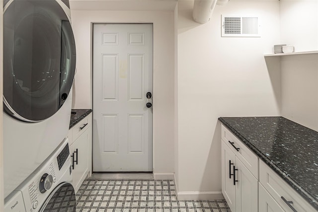 laundry room featuring cabinet space, baseboards, visible vents, and stacked washer / dryer