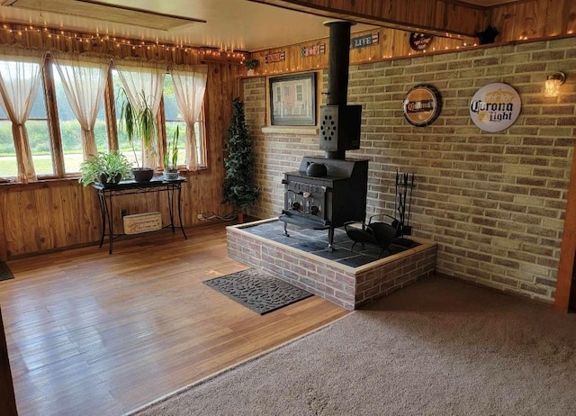 living room featuring hardwood / wood-style floors, a wood stove, wooden walls, and brick wall