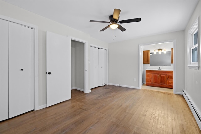 unfurnished bedroom featuring ceiling fan, baseboard heating, light hardwood / wood-style flooring, ensuite bathroom, and two closets