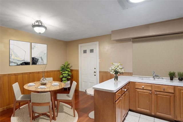 kitchen with light wood-type flooring, kitchen peninsula, sink, and wooden walls