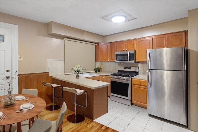 kitchen featuring sink, light wood-type flooring, appliances with stainless steel finishes, tasteful backsplash, and kitchen peninsula