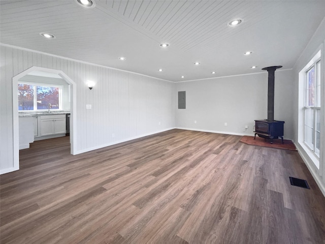 unfurnished living room featuring ornamental molding, dark wood-type flooring, electric panel, a wood stove, and wood walls