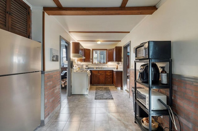 kitchen featuring ornamental molding, stainless steel refrigerator, beamed ceiling, white range oven, and brick wall