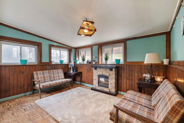 living area featuring crown molding, vaulted ceiling, wooden walls, a fireplace, and light parquet flooring