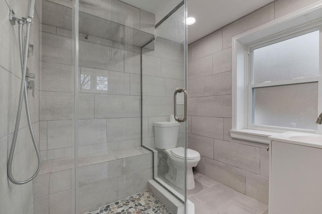 bathroom with walk in shower, tile patterned floors, toilet, vanity, and tile walls