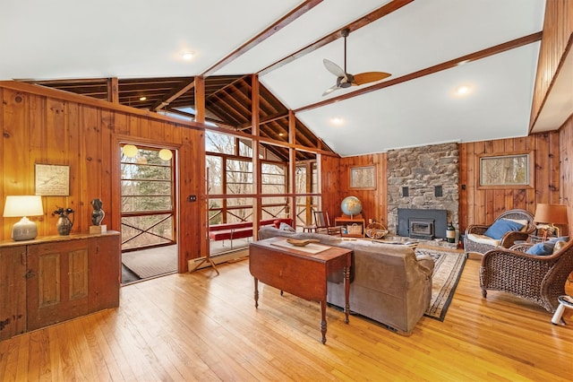 living room with baseboard heating, wooden walls, vaulted ceiling with beams, light hardwood / wood-style floors, and a wood stove