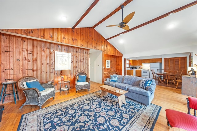 living room with light wood-type flooring, lofted ceiling with beams, ceiling fan, and wooden walls