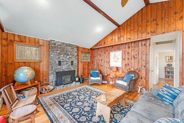 living room with wood walls, a wood stove, ceiling fan, light wood-type flooring, and beam ceiling