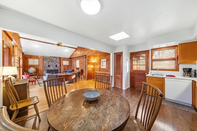 dining room with light wood-type flooring, sink, a stone fireplace, lofted ceiling, and wood walls