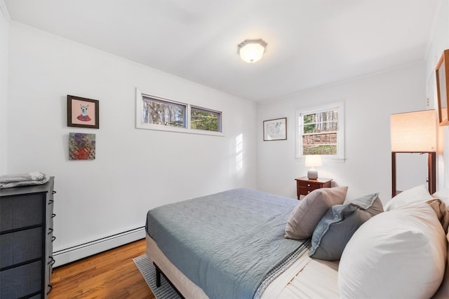 bedroom with light hardwood / wood-style floors, ornamental molding, and a baseboard heating unit