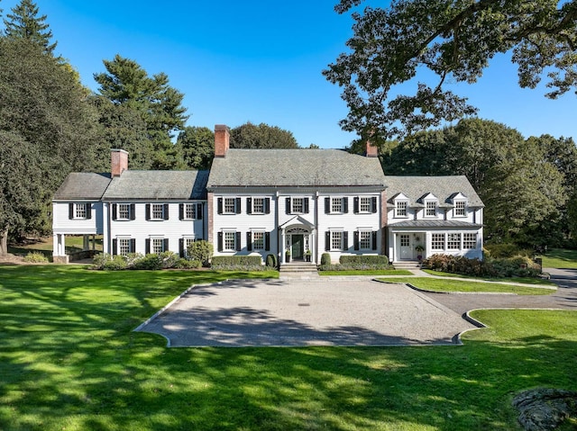 view of front of home featuring driveway, a chimney, and a front lawn