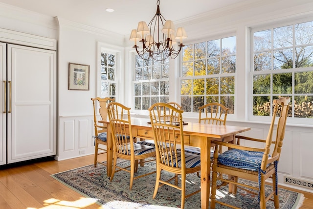 dining room featuring light wood finished floors, plenty of natural light, crown molding, and wainscoting